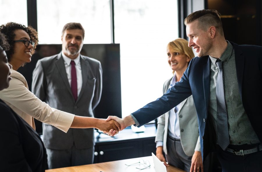 man and woman shake hands over a wooden table with people in background