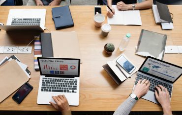 many people working with laptops, date books and drinks at a group table