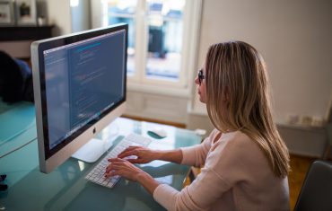 woman sits inside at home at a desktop computer