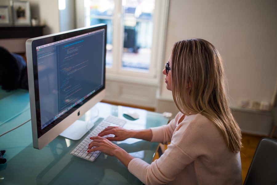 woman sits inside at home at a desktop computer